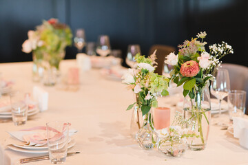 Coziness and style. Modern event design. Table setting at wedding reception. Floral compositions with beautiful flowers and greenery, candles, laying and plates on decorated table.