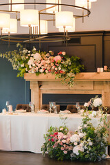 Coziness and style. Modern event design. Table setting at wedding reception. Floral compositions with beautiful flowers and greenery, candles, laying and plates on decorated table.