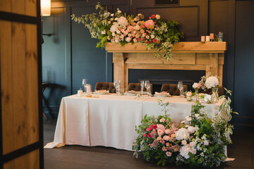 Coziness and style. Modern event design. Table setting at wedding reception. Floral compositions with beautiful flowers and greenery, candles, laying and plates on decorated table.