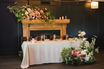 Coziness and style. Modern event design. Table setting at wedding reception. Floral compositions with beautiful flowers and greenery, candles, laying and plates on decorated table.