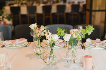 Coziness and style. Modern event design. Table setting at wedding reception. Floral compositions with beautiful flowers and greenery, candles, laying and plates on decorated table.
