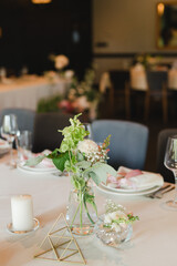 Coziness and style. Modern event design. Table setting at wedding reception. Floral compositions with beautiful flowers and greenery, candles, laying and plates on decorated table.