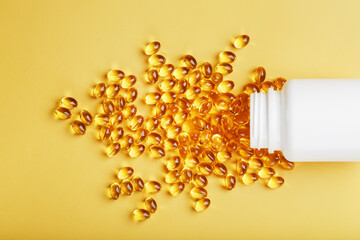 Golden Omega-3 fish oil capsules poured out of a jar on a yellow background