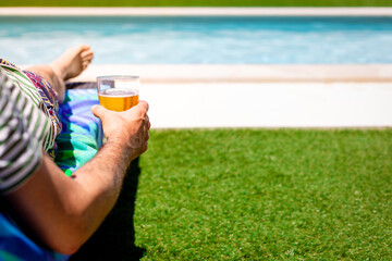 Man relaxing lying on a sun lounger by the pool with a beer in hand