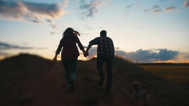 happy family couple and dog runs hands jumping up for joy at sunset on a hilltop and jumps. concept of team business concept travel freedom victory happiness teamwork. happy family parents hold hands