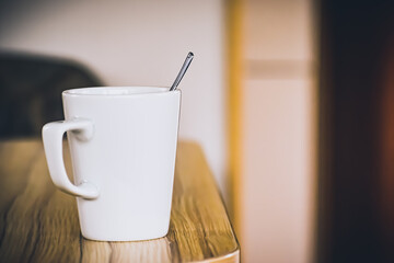 A white cup with stirring spoon resting inside