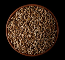 Spelt grains in clay pot, bowl isolated on black, top view