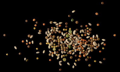 Mixed legumes and cereals, peeled barley, green, yellow and dark red lentils, half green peas, black white beans, green beans in clay pot isolated on black, top view