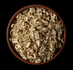 Pile dry chopped parsnip root in clay pot isolated on black