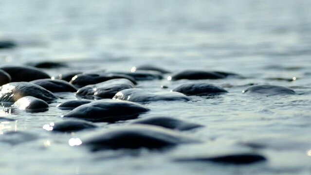 The Baltic Sea with calm water splashes over the rocks in slow motion and reflects glitter during the sunset, the film is in soft toning with space for text