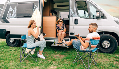 Group of friends with their dog drinking beer in front of their camper van