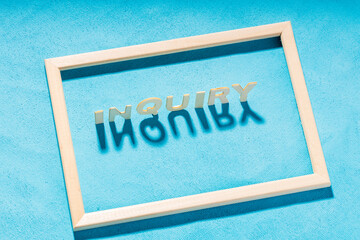 inquiry word from wooden letters cast away inside a wooden frame on a blue background