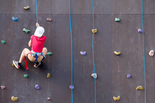 child rock climber holding onto a rope at a climbing training stand