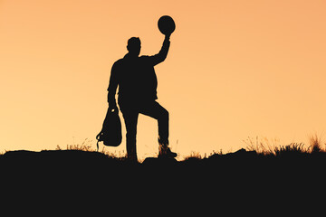 the silhouette of man who greets by raising his hat. greeting sign on orange background