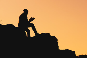 silhouette of a man in a hat reading a book. solitude and reading books in nature