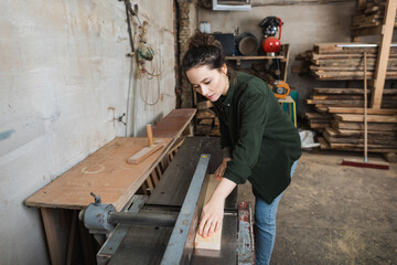 Carpenter working with plank and jointer machine in workshop.