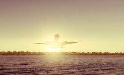 Airplane over the forest and the river. Transport and travel. Shining bright yellow sun - Powered by Adobe