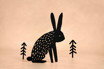 Cute Black Bunny and Trees on a Grunge Light Beige Background. Funny Modern Minimalist Easter Holiday Composition with Rabbit ideal for Banner, Card, Greetings. No text. Woodland Art.