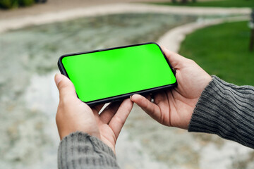 Girl in the park holding a smartphone with Green screen. Wooden bridge, green area and an...