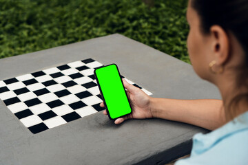Girl in the park holding a smartphone with Green screen. Cement table. Chroma Key