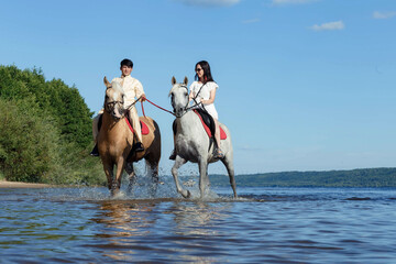 a guy and a girl on horseback on a river on a sunny day