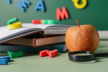 Books, magnifier, apple and colorful letters on table in classroom, closeup