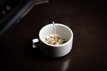 Herbal tea in a cup. Brewing a drink from different herbs in a white cup on a dark background.