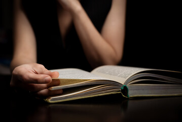 A woman is reading a book in the dark. Sits by the table.