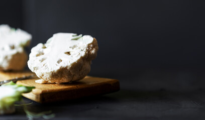 Cauliflower on a wooden cutting board. Dark background. Place for text. Side view.