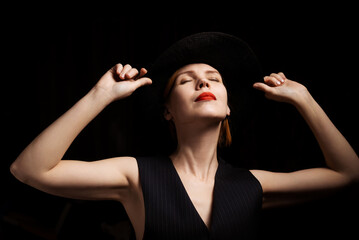 Middle-aged woman in a hat on a black background. A lovely woman in her forties. Dreaming, fantasy concept.