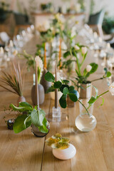 Coziness and style. Modern event design. Table setting at wedding reception. Floral compositions with beautiful flowers and greenery, candles, laying and plates on decorated table.