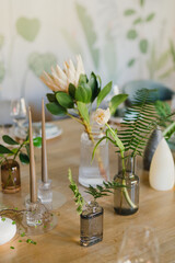 Coziness and style. Modern event design. Table setting at wedding reception. Floral compositions with beautiful flowers and greenery, candles, laying and plates on decorated table.