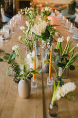 Coziness and style. Modern event design. Table setting at wedding reception. Floral compositions with beautiful flowers and greenery, candles, laying and plates on decorated table.