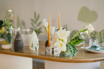 Coziness and style. Modern event design. Table setting at wedding reception. Floral compositions with beautiful flowers and greenery, candles, laying and plates on decorated table.