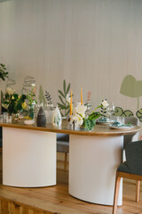 Coziness and style. Modern event design. Table setting at wedding reception. Floral compositions with beautiful flowers and greenery, candles, laying and plates on decorated table.