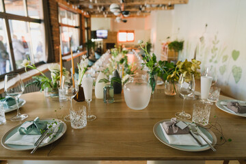 Coziness and style. Modern event design. Table setting at wedding reception. Floral compositions with beautiful flowers and greenery, candles, laying and plates on decorated table.