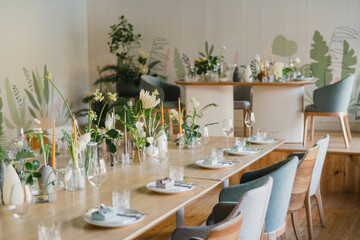 Coziness and style. Modern event design. Table setting at wedding reception. Floral compositions with beautiful flowers and greenery, candles, laying and plates on decorated table.