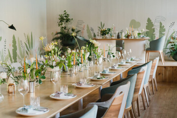 Coziness and style. Modern event design. Table setting at wedding reception. Floral compositions with beautiful flowers and greenery, candles, laying and plates on decorated table.