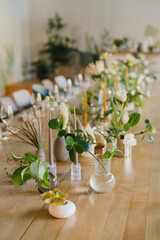 Coziness and style. Modern event design. Table setting at wedding reception. Floral compositions with beautiful flowers and greenery, candles, laying and plates on decorated table.