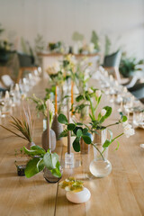 Coziness and style. Modern event design. Table setting at wedding reception. Floral compositions with beautiful flowers and greenery, candles, laying and plates on decorated table.