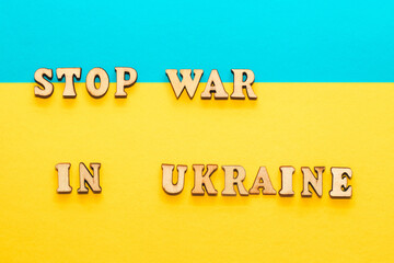 Wooden inscription stop war in ukraine on a cardboard yellow-blue background of the flag of ukraine.