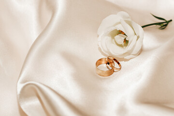 Obraz na płótnie Canvas White rose on a silk beige background with gold jewelry wedding rings, space for text.
