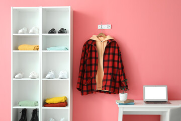 Interior of room with workplace, shelf unit and hoodie hanging on wall