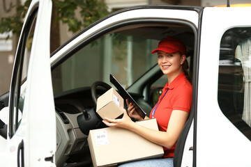 Female courier of delivery company with parcels in car - obrazy, fototapety, plakaty