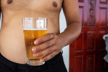 chubby young man held glass of beer in his hand, and his fattening figure was caused by drinking too much beer and becoming obese. The concept of health care by losing weight for good health