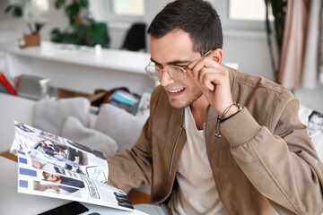 Young man in eyeglasses with magazine sitting at table in cafe