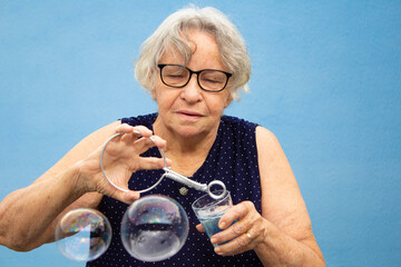 Mulher idosa fazendo bolhas de sabão com fundo azul.