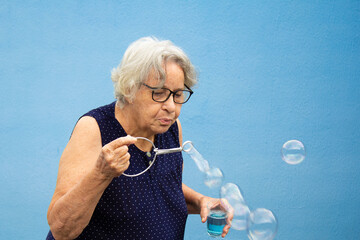 Mulher idosa fazendo bolhas de sabão com fundo azul.