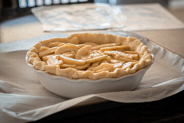 Mom is making homemade apple pie and rolled out the crust and put it into the pie plate with the cinnamon and sugar-coated sliced apples