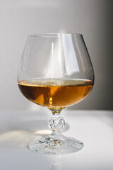 brandy snifter on white reflective table with white background by window